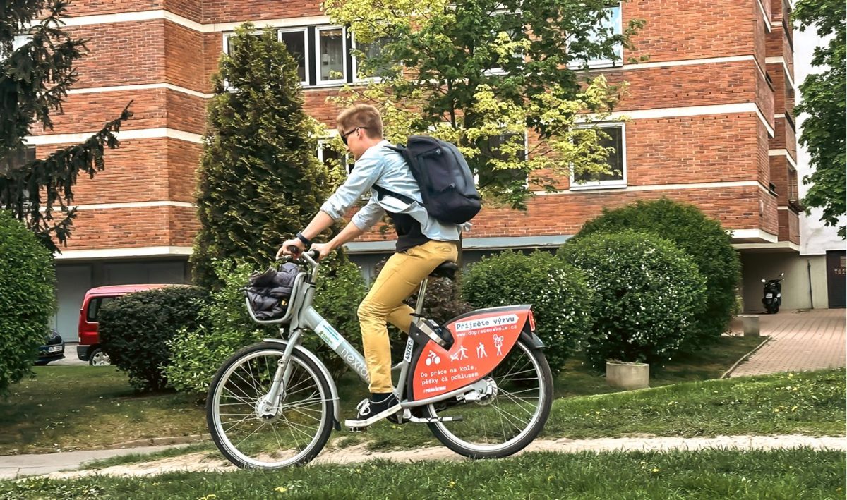 Cyklista s batohem jede na kole nextbike s polepem výzvy Do práce na kole